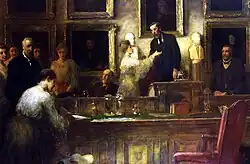 a colour painting of men and women in formal Edwardian dress, standing around (and one woman seated at) a boardroom table