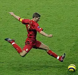 Gerrard wearing an all-red kit and powerfully kicking a yellow ball in a match