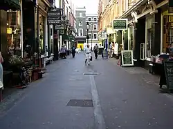 Narrow street with shops on each side. A few people are walking or window-shopping.