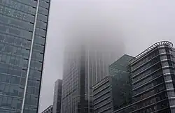 A large building heads up into the sky. Only a portion of the building is visible, as the top is engulfed in a thick fog.
