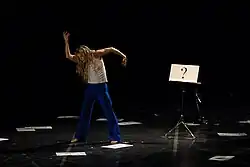 Louise Lecavalier performing in Pite's work "Lone Epic." Beside the dancer is a music stand with sheet of paper displaying "?".