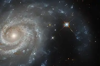 A large spiral galaxy seen close-up. The left side of the image shows the galaxy's core and its tightly-curled inner spiral arms. On the right side, one of the arms reaches down from above, curving across the dark background. There is a bright star inside the arc of the arm, and a couple more next to the galaxy.