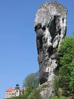 The Cudgel of Hercules, a tall limestone rock formation, with Pieskowa Skała Castle in the background