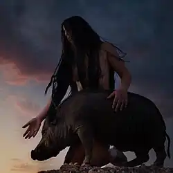 A photo of a person with long hair kneeling next to a hog