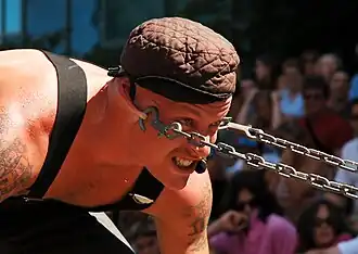 A man bent forward with chains hooked to his earlobes