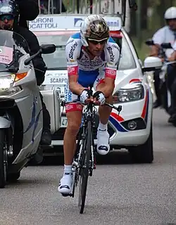 A solo cyclist competing in a time trial, being followed by a motorcyclist and a team car