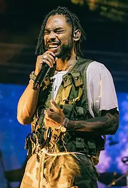 Miguel performing in a white shirt with a green vest and pants.