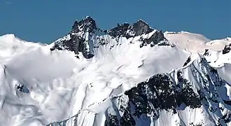 A dark rugged mountain towering over glacial ice and rock on a clear day.