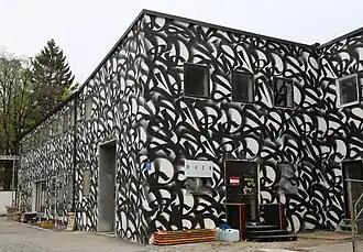 Low, flat former substation building with black-and-white abstract lettering on the exterior