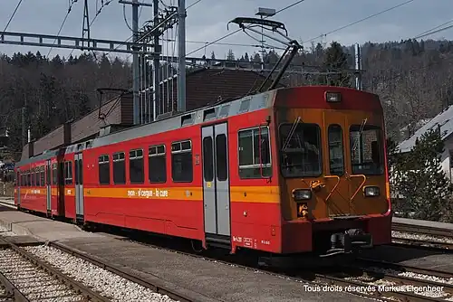Red and orange train on a railway line next to a platform