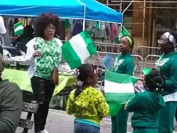 A group of people in green and white outfits hold Nigerian flags at an outdoor event