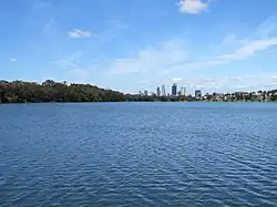 A lake with a city skyline in the background and trees to the left