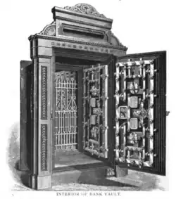 A black-and-white photo of the interior side of the Ocean National Bank's vault room entrance. There are two doors at both ends of a wooden recessed entrance, and the inner door is opened to show the entrance and the outer door, which is closed. Both doors are made of iron and have combination locks. The frame of the inner door is wooden and made in the Victorian style.