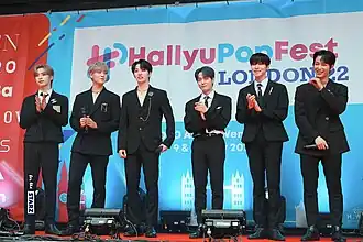 Oneus in London for a K-pop festival, standing on a red carpet in black suits.