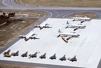 An aerial view of Royal Australian Air Force (RAAF) fighters, Royal New Zealand Air Force (RNZAF) and United States Navy (USN) patrol aircraft (bottom to top) parked on a ramp during exercise Sandgroper 1982. Visible are seven Dassault Mirage IIIO and one Mirage IIID of No. 77 Squadron RAAF, two Lockheed P-3C Orion aircraft of No. 10 Squadron RAAF, one Lockheed P-3B Orion of No. 5 Squadron RNZAF, and two P-3B (BuNos 152733 and 153418) of Patrol Squadron VP-1 Screaming Eagles, USN.
