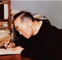 An elderly man at his desk, writing