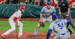Baseball players wearing caps; the player in red wears a batting helmet