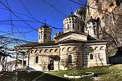 Side view of a three-domed Orthodox church with blind arches. Cliffs in the background.