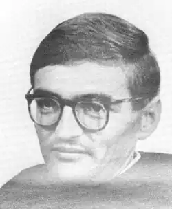 A photograph of a white man with hair, glasses, and a sweater shown from the shoulders up.