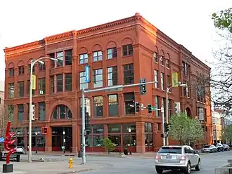 A large four-story red brick building with many windows. The building is on a street corner with the front and one of the sides visible.