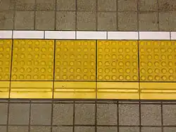 Tactile pavings installed on a platform at a Japanese train station. Horizontal tactile paving at the bottom indicates the 'inner' side, away from the rail tracks.