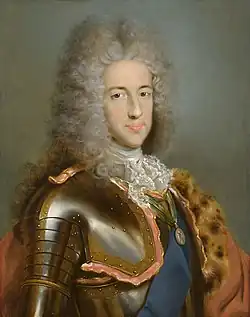 A young man wears a powdered wig while posing in a suit of armour.