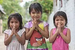 Group portrait photograph at bust length of three Lao girls joining their palms for the Thai greeting (Namaste).