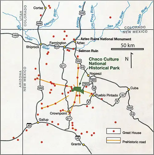 Large square map of northwestern New Mexico and neighboring parts of, clockwise from left, western Arizona, southeastern Utah, and southwestern Colorado. The map region has a green and blocky rectangular-crescent area at its center labeled Chaco Culture National Historical Park. Radiating from the green region are seven segmented gold lines: "[p]rehistoric roads", each several dozen kilometers in length when measured according to the map scale factor. Roughly seventy red dots mark the location of great house[s]; they are widely spread across the map, many of them far from the green area, near the extremes of the map, more than one hundred kilometers from the green area. Two proceed roughly south, one southwest, one northwest, one straight north, and the last to the southeast. Yellow dots mark the location of modern settlements: Shiprock, Cortez, Farmington, and Aztec to the northwest and north; Nageezi, Cuba, and Pueblo Pintado to the northeast and east; Grants, Crownpoint, and Gallup to the south and southwest. They are connected by a network of gray lines marking various interstate and state highways. A fan of thin blue lines along the northern margins of the map depict the San Juan River and its communicants.