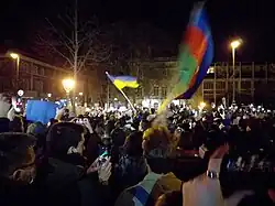 Hungarians demonstrate in Budapest at the onset of the Russian invasion of Ukraine in a public square at night, waving a Ukrainian flag