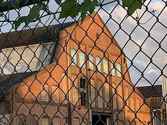 A large brick train shed seen through a chain-link fence