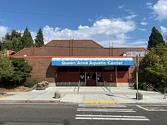 A modern photograph of the Queen Anne Pool, a brick building with a stepped roof and a large blue awning