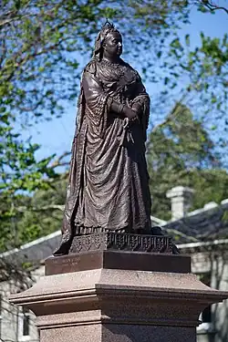 A bronze statue of Queen Victoria atop a granite pedestal, holding a fan.