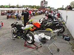 Pre-race assembly area[2] adjacent to startline showing machines with tyre warmers plugged into wall-mounted electrical outlets
