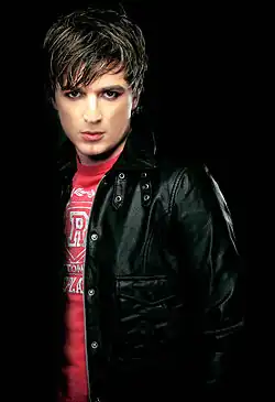 Portrait of Radu Sîrbu, wearing a red shirt and a black jacket against a dark background.