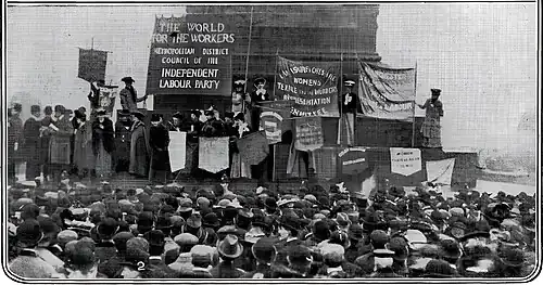 a group of speakers are on the raised plinth of Nelson's Column, in front of a large crowd