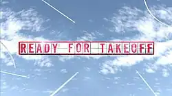 The words Ready for Take Off spelled out as separate letters on a display board, as aircraft in the distance fly around.