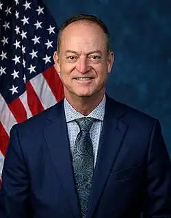 Official House portrait of Messmer smiling in front of the U.S. flag, wearing a dark blue suit, dotted white and blue shirt, and floral green and dark blue tie.