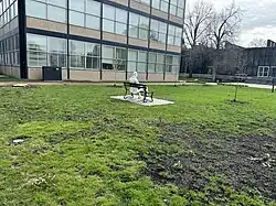 Reverse of the Man on a Bench sculpture from a distance. Wishnick Hall is in the background.