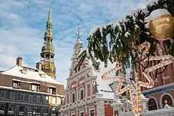 A picture of a Christmas ornament on a Christmas tree at the Riga Town Hall square, with House of the Blackheads in the background.