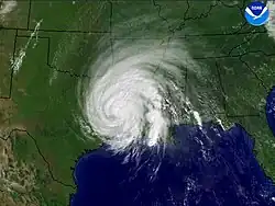 A satellite view of Hurricane Rita, rotating counterclockwise, over Louisiana and Mississippi. The hurricane appears as a white circular cyclone at the center of the image; the Gulf of Mexico is visible below it. At the top-right corner of the image is the logo of the National Oceanic and Atmospheric Administration.