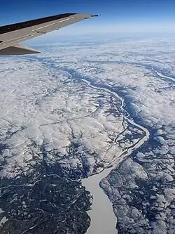 An aerial photo viewing down to Earth with rivers visible. Ground is covered by snow, with trees in the lower left and in the valleys of the rivers.