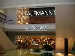 A two-story shopping mall concourse leading to a department store. Present are two signs reading "Kaufmann's"