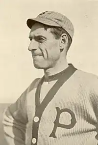 A sepia-toned image of a man wearing a button-down sweater with a "P" on the left breast and a crownless pinstriped baseball cap
