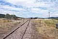 Looking east along the railway line from level crossing on Bylong Valley Way near Sandy Hollow, showing rear end of train waiting on crossing loop