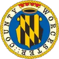 A round seal featuring a yellow-and-black shield on a blue background with a white-and-yellow border