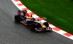 A navy blue Formula One car being driven at speed on a dry race track