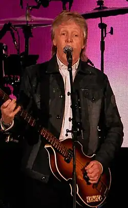 Paul McCartney playing a guitar and singing onto a mic