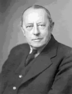 Black and white portrait photo of middle-aged white man, clean shaven, receding hair, in formal suit and tie