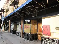 Photograph of the exterior of a two-story brick building with boarded windows and graffiti