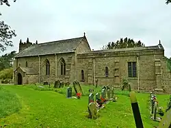 A church with a low roof, with a mowed grass section and gravestones in front